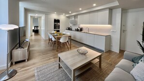 Un espacio moderno y abierto para sala y comedor, con cocina, piso de madera y televisor de pantalla plana.