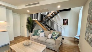 Una sala de estar moderna con un sofá color beige, una mesa de centro de madera y una escalera con barandas negras.