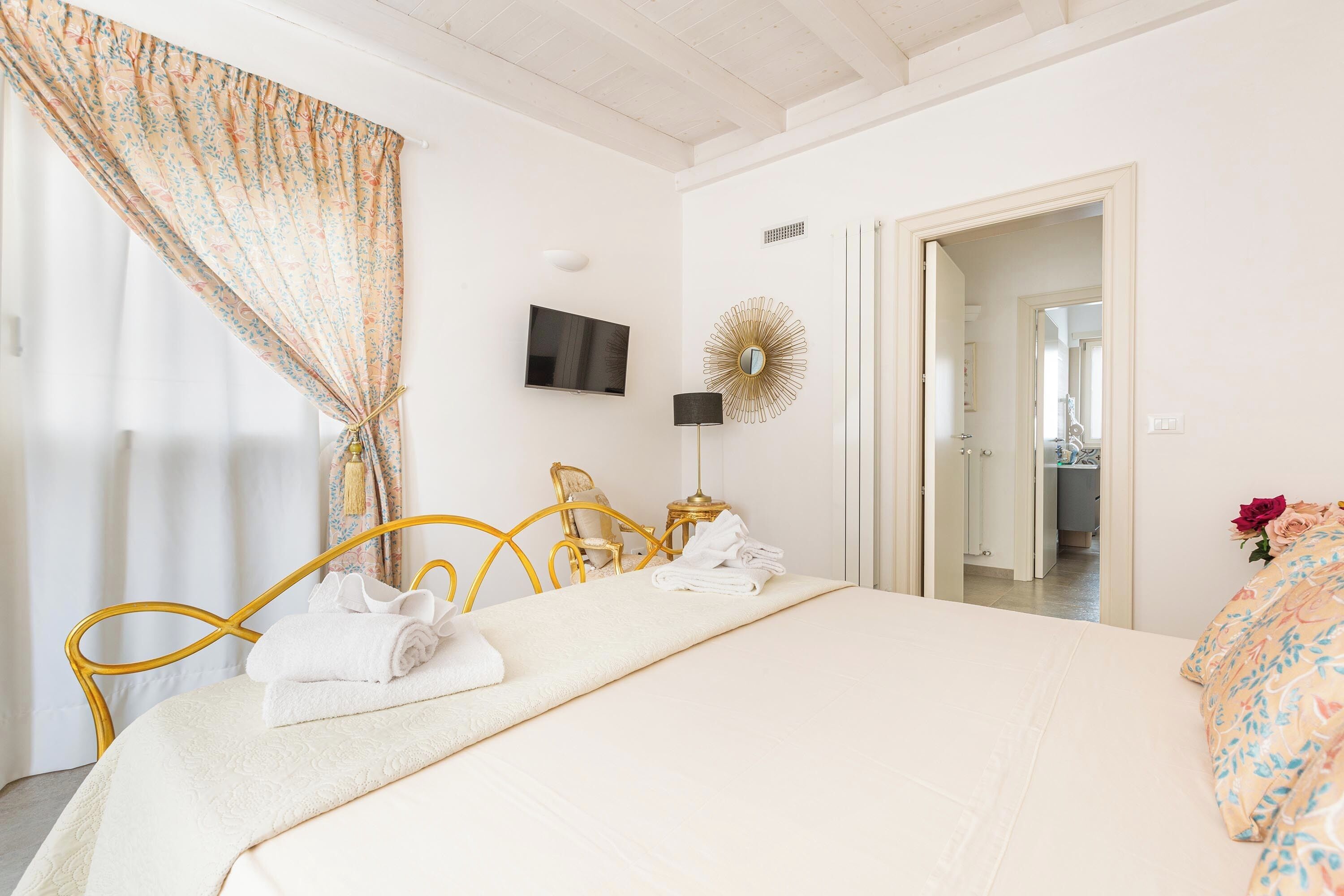 A hotel room with a bed, a television, a lamp, and a door leading to another room.
