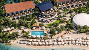 An aerial view of a resort with a pool, beachside lounge, and a circular building with outdoor seating. - Kalkan Beach Park Hotel (Kas)