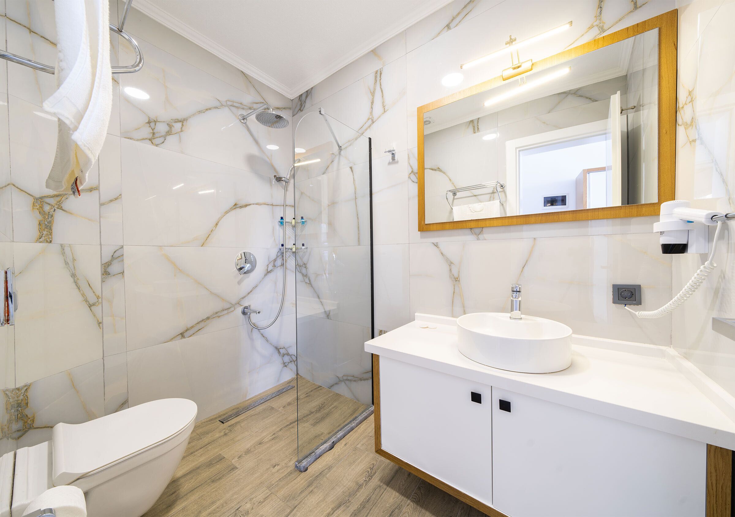 A modern bathroom with a glass shower enclosure, a white sink, and a marble-tiled wall.