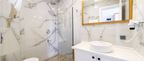 A modern bathroom with a glass shower enclosure, a white sink, and a marble-tiled wall.
