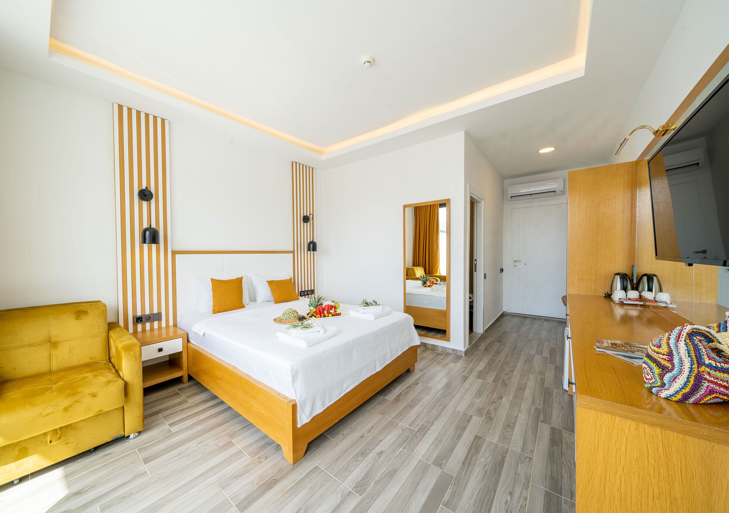 A modern hotel room with a bed, a sofa, a desk, and a mirror.