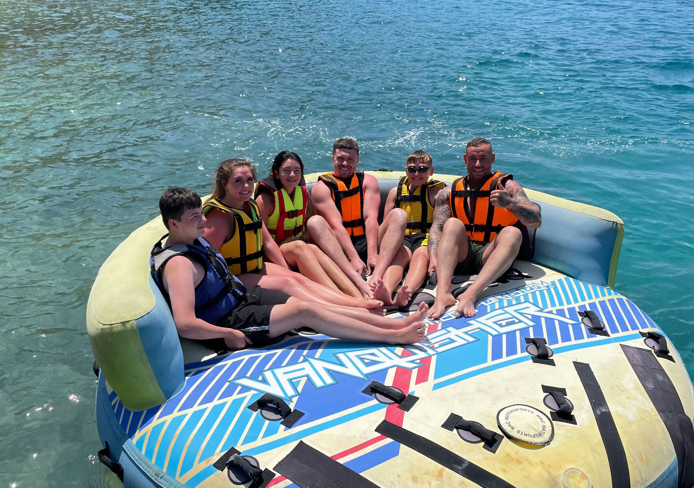 A group of people on a watercraft with life jackets, a steering wheel, and a steering wheel label.