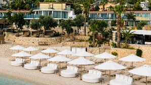 A beachside hotel with multiple round white sunbeds and umbrellas, stone walls, and a clear view of the sea. - Kalkan Beach Park Hotel (Kas)