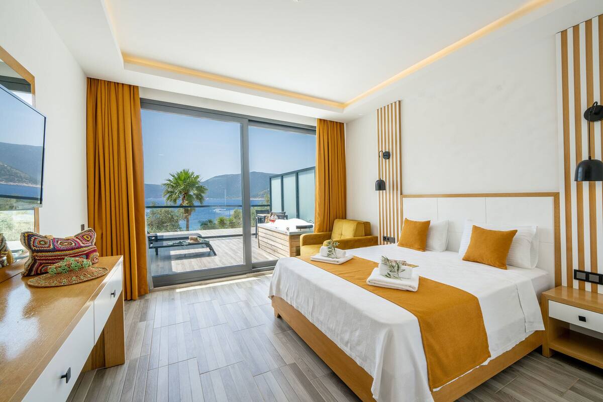 A modern hotel room with a large bed, a desk, a chair, and a balcony with a view.