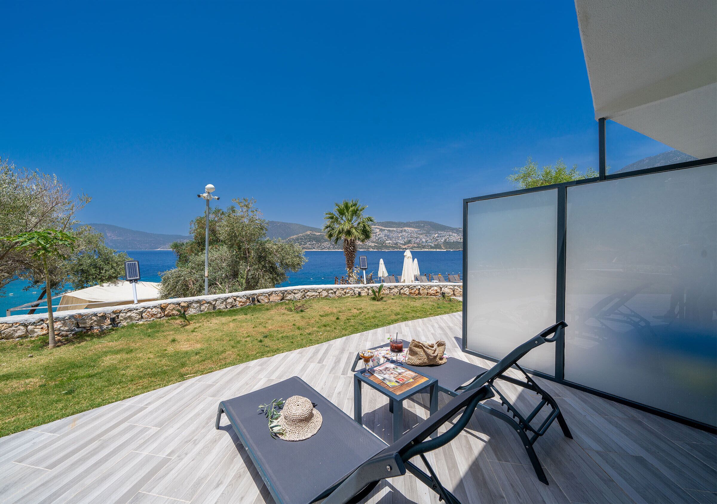 A balcony with a view of the sea, a table with a hat, a magazine, and a drink.