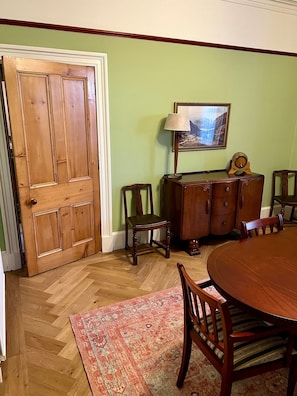 Un comedor con una mesa de madera, sillas, un tapete, un armario y un cuadro en la pared.