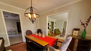 A dining area with a wooden table, red tablecloth, and a chandelier. There are chairs around the table, and a patterned rug on the floor.