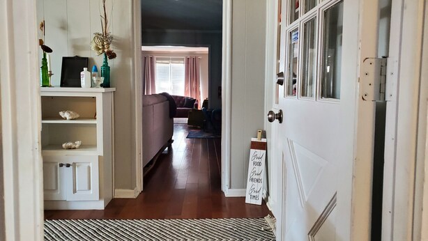 A hallway leading to a living room with a sofa and a window with curtains.