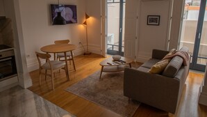 Moderni olohuone, jossa on puinen ruokapöytä, sohva ja suuri ikkuna, josta tulee runsaasti luonnonvaloa.