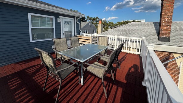 A covered patio with a glass table and chairs, a white railing, and a brick chimney.