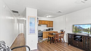Un espacio habitable compacto con kitchenette, comedor y televisor montado en la pared.