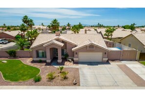 Two-story house with a flat roof and garage, set amidst a well-maintained lawn and gravel driveway.