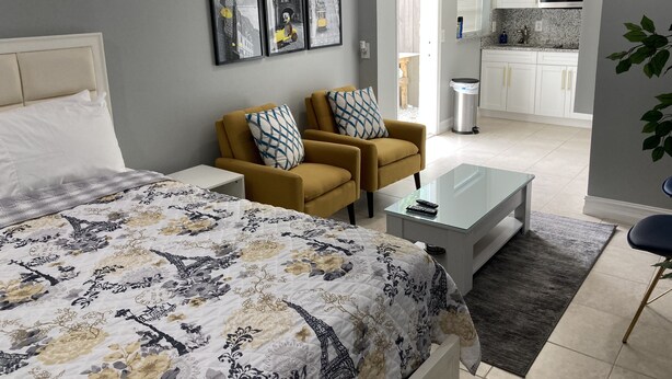 A bedroom with a bed, two armchairs, a coffee table, and a view into the kitchen. - Cottage totally private detached 1 queen bed private patio (West Palm Beach)