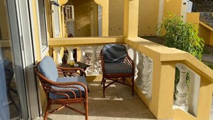 Ein Balkon mit zwei Korbstühlen und einem kleinen Tisch, gelben Wänden und einem weißen Geländer.