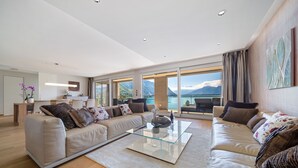 A modern living room with a glass coffee table, beige sofas, and a view of mountains and water. - Montreux Panoramic Views 4BD Apartment (Montreux)