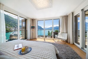 A bedroom with a large bed, a view of a lake, and a balcony with outdoor furniture.
