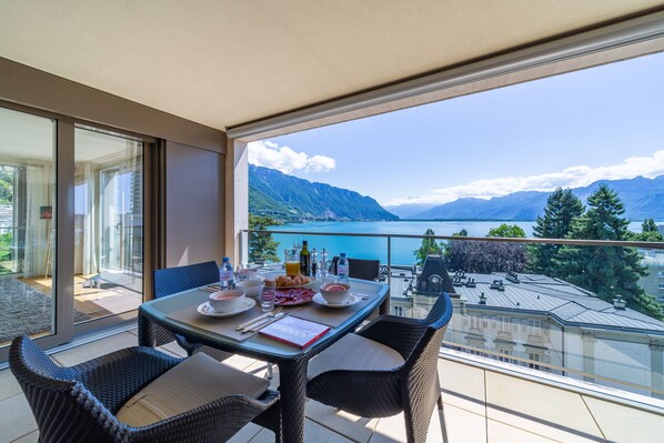 A balcony with a table set for breakfast, overlooking a lake and mountains.