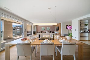 A modern dining area with a wooden table set for four, surrounded by chairs. A large window offers a view of mountains.