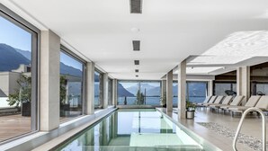 A modern indoor swimming pool with clear glass walls, a view of mountains, and a lounge area with chairs. - Montreux Panoramic Views 4BD Apartment (Montreux)