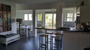 Een moderne keuken met een centraal eiland, barstoelen en een eethoek met een witte tafel en stoelen.