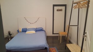 Een slaapkamer met een bed, een stoel, een kledingkast en een kleine tafel met een lamp.