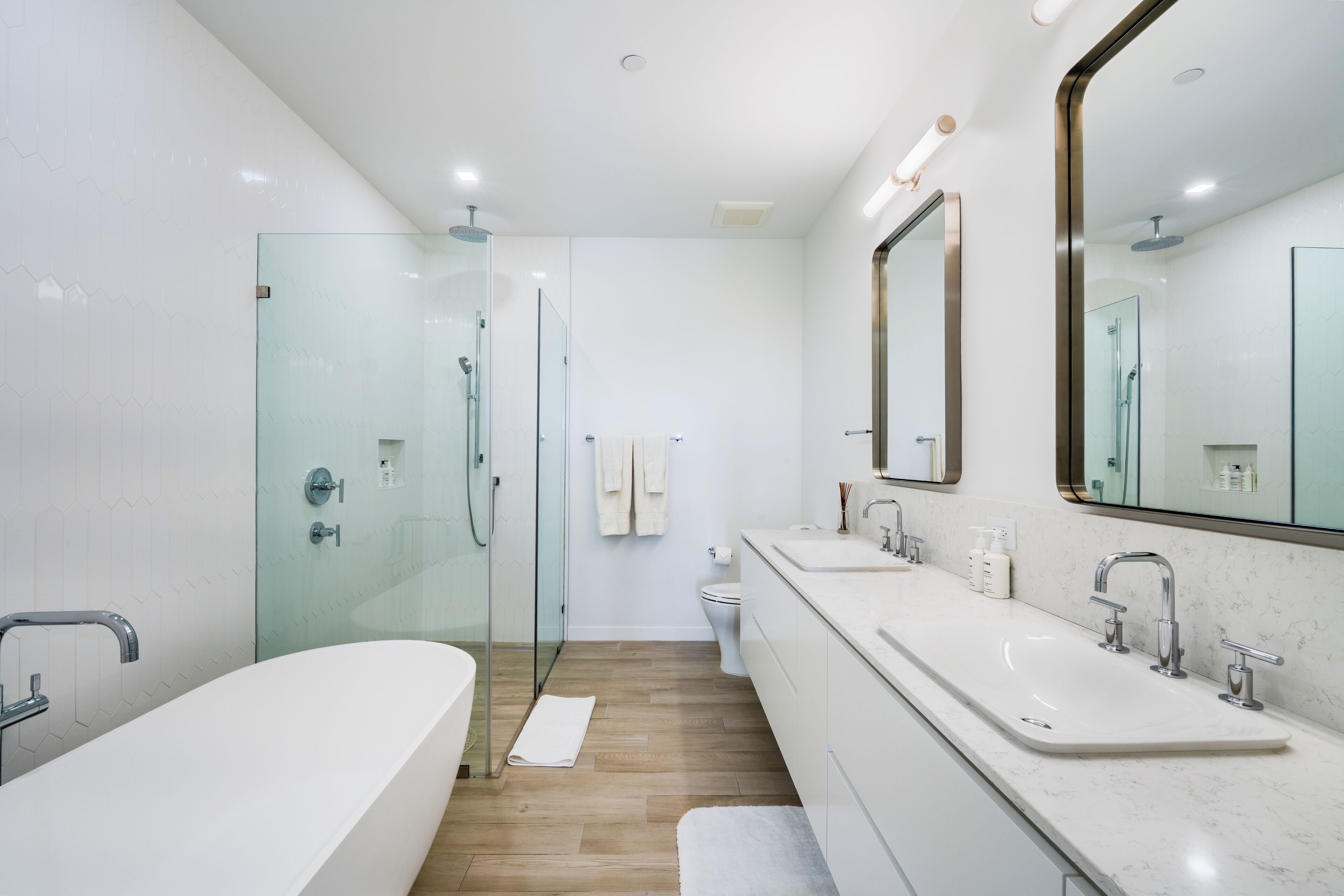 Un baño moderno con ducha envuelta en vidrio, una bañera amplia y un tocador doble.