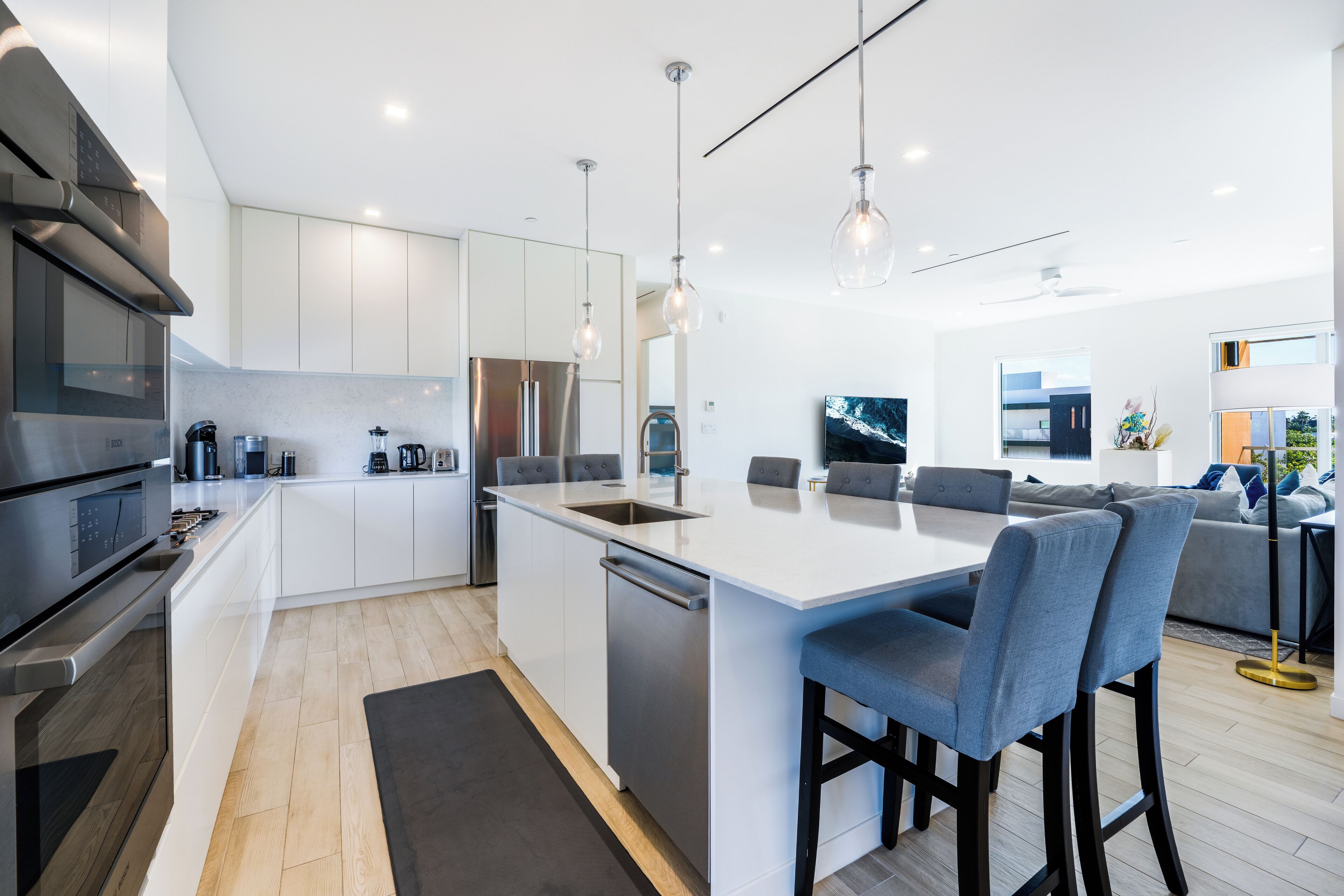 A modern kitchen with white cabinetry, stainless steel appliances, and a central island with bar stools.
