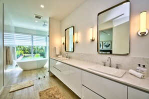 A modern bathroom with a large bathtub, two sinks, and a large mirror.