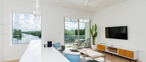Una cocina moderna con una isla grande, un comedor con vistas a un lago y un televisor montado en la pared.
