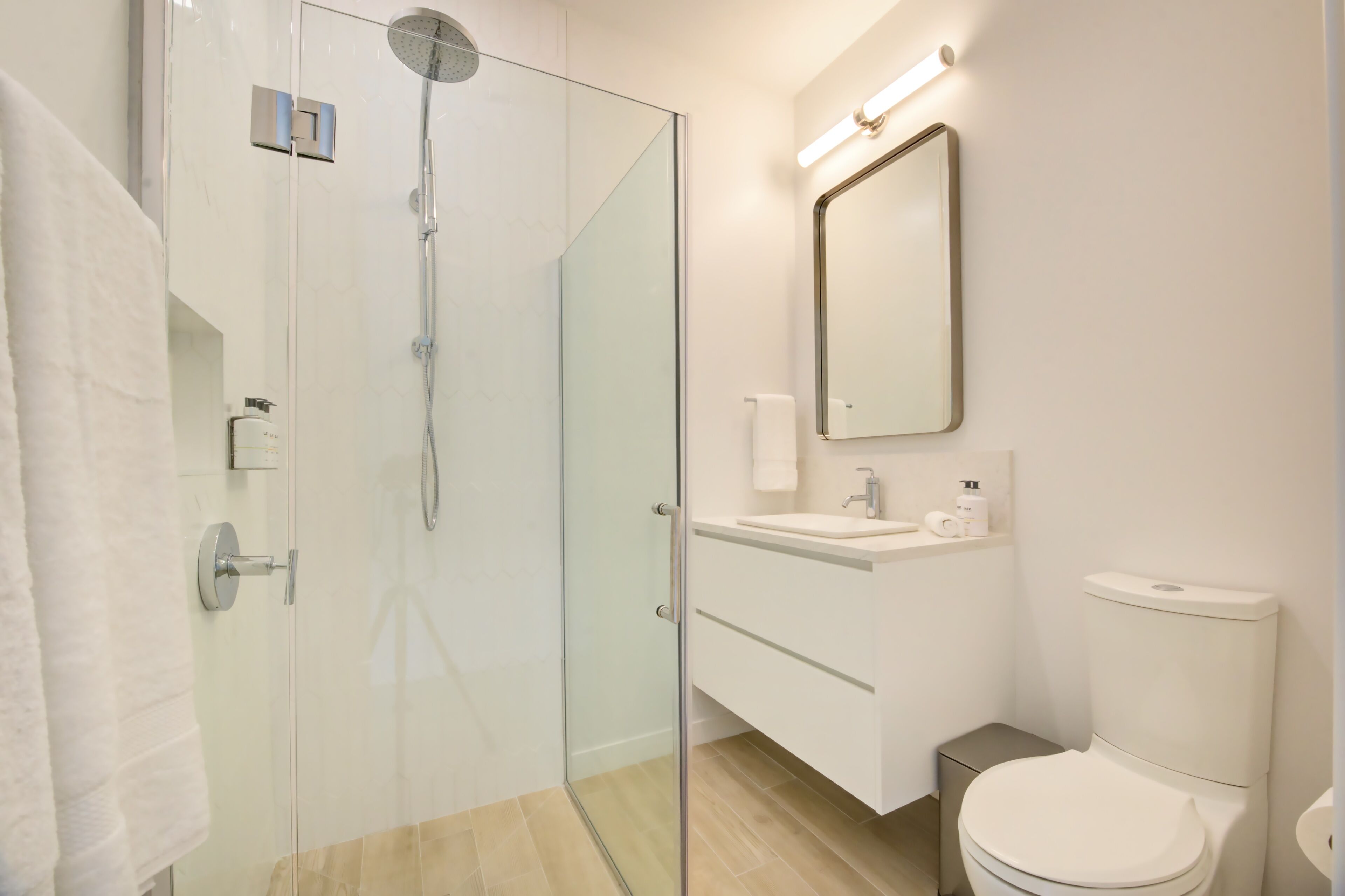 Un baño moderno con ducha envuelta en vidrio, un lavabo blanco, un inodoro y un espejo.