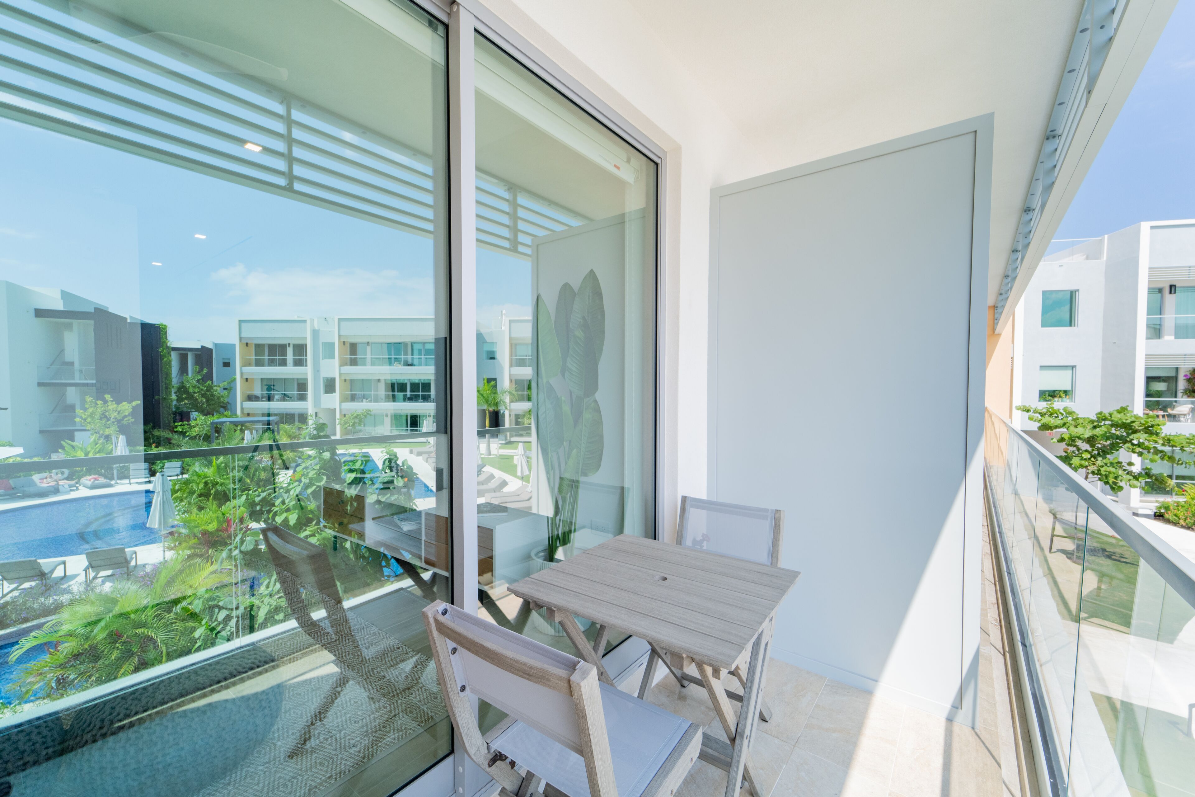 A balcony with a table and chairs, overlooking a swimming pool and greenery.