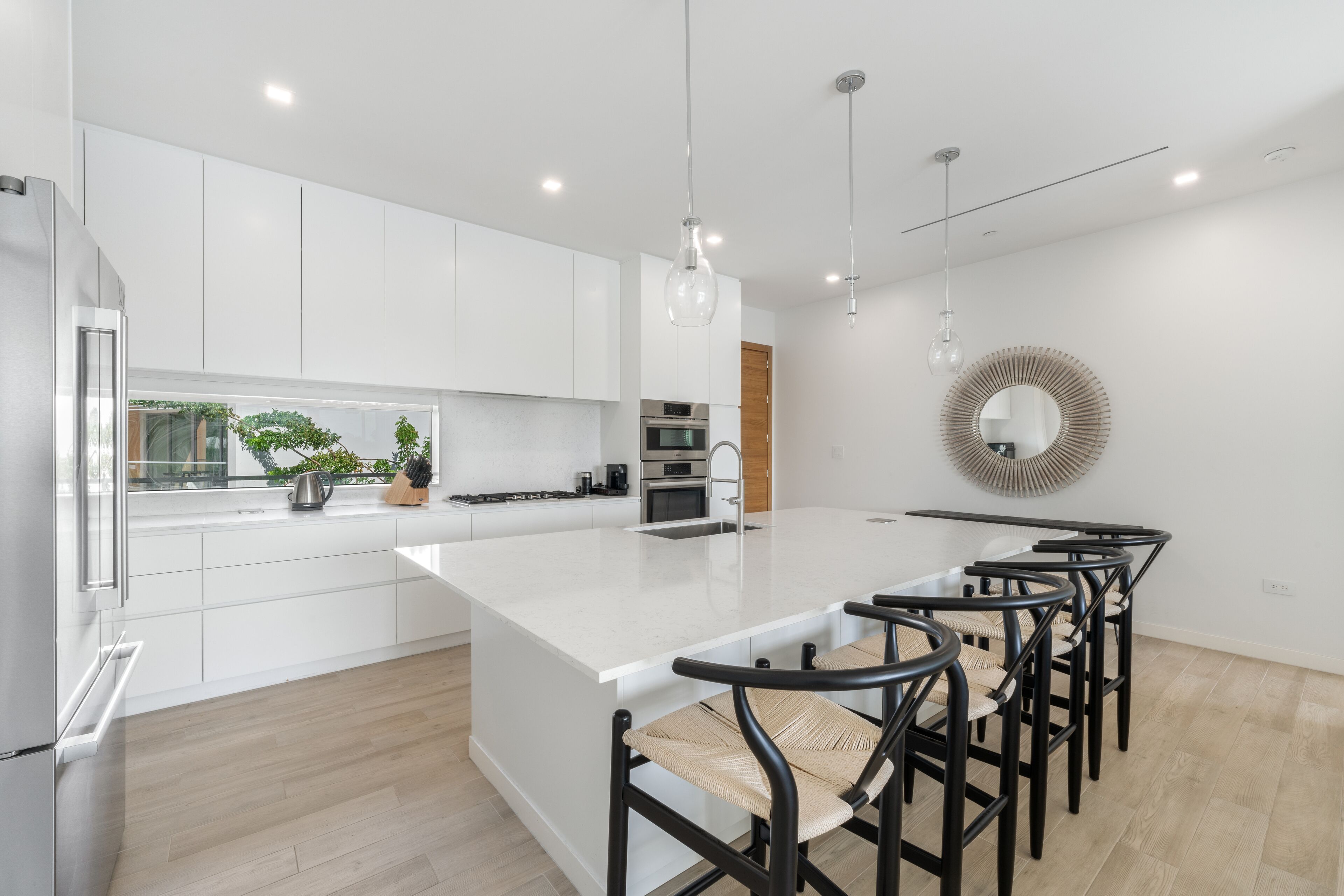 Una cocina moderna con muebles blancos, una isla grande y un comedor con sillas negras.