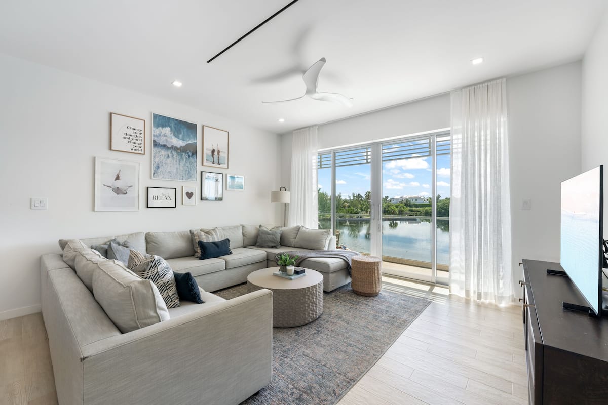 A modern living room with a large window, a ceiling fan, and a flat-screen TV.