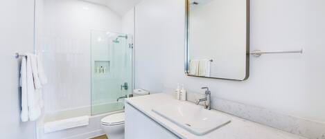 Een moderne badkamer met een douchecabine van glas, een wit wastafeltje en een grote spiegel.