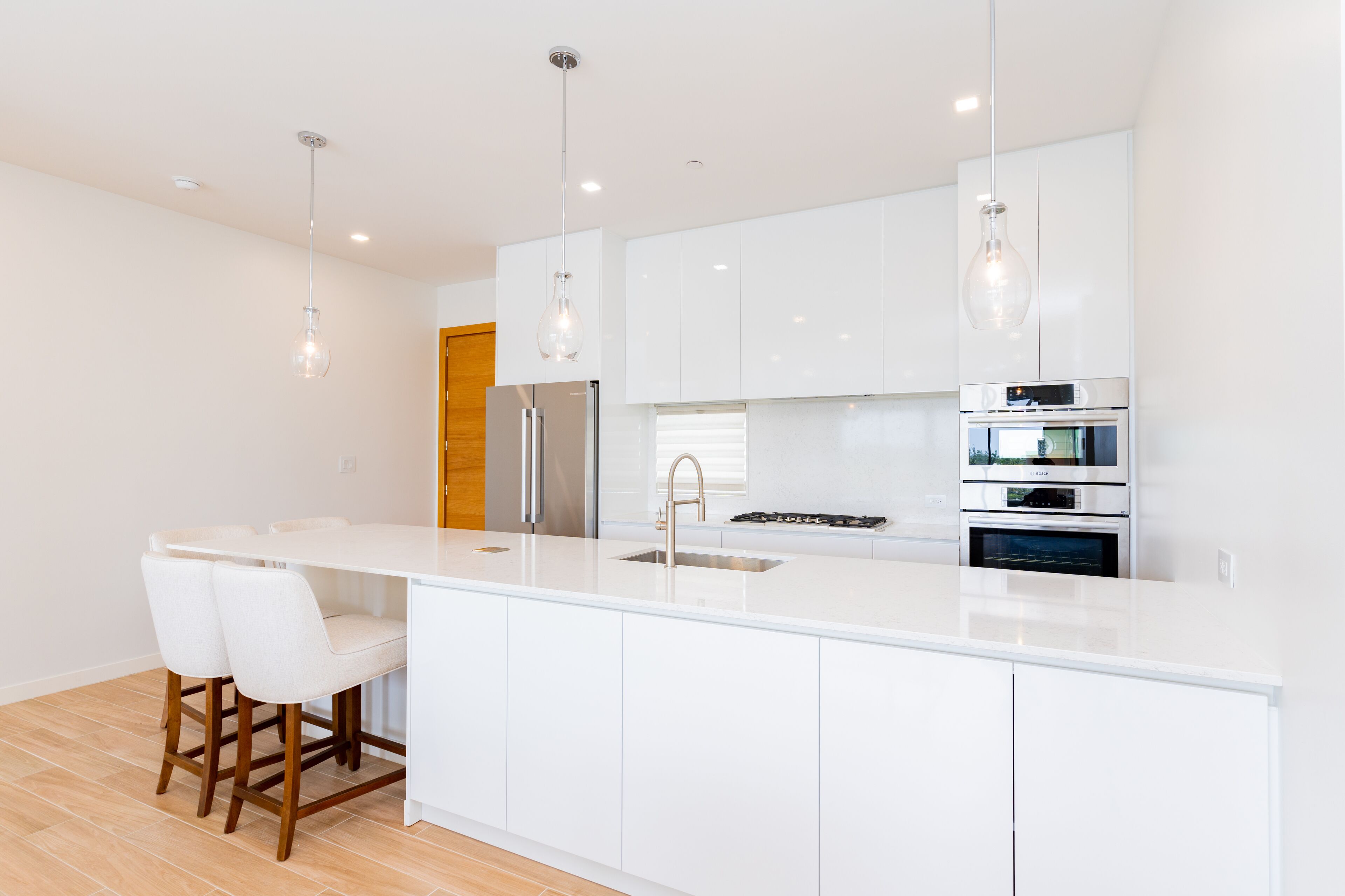 A modern kitchen with white cabinetry, stainless steel appliances, and pendant lighting.