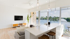 A modern kitchen with a large island, bar stools, and a view of a lake. - ONE Canal Point (Seven Mile Beach)