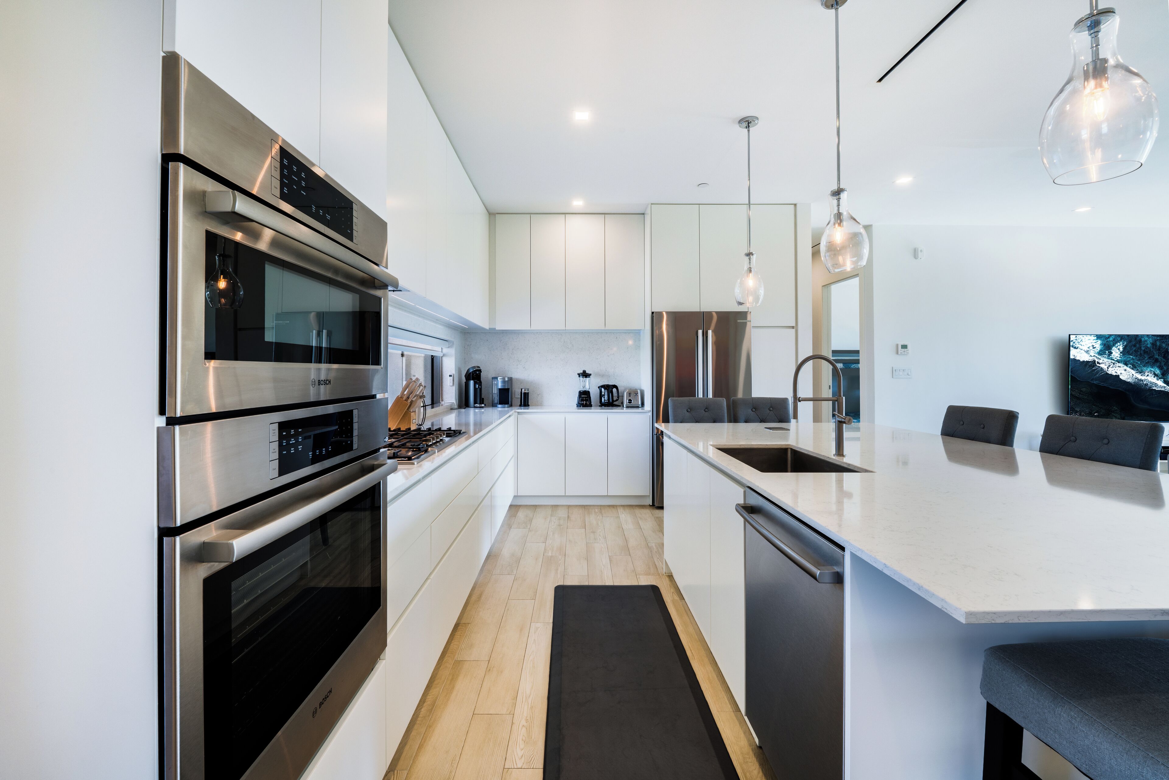 Une cuisine moderne dotée d’appareils électroménagers en acier inoxydable, d’un îlot central et de luminaires suspendus.
