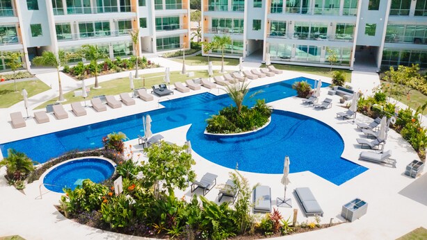 A modern hotel with a large outdoor swimming pool, multiple lounge areas, and a well-maintained garden. - ONE Canal Point (Seven Mile Beach)