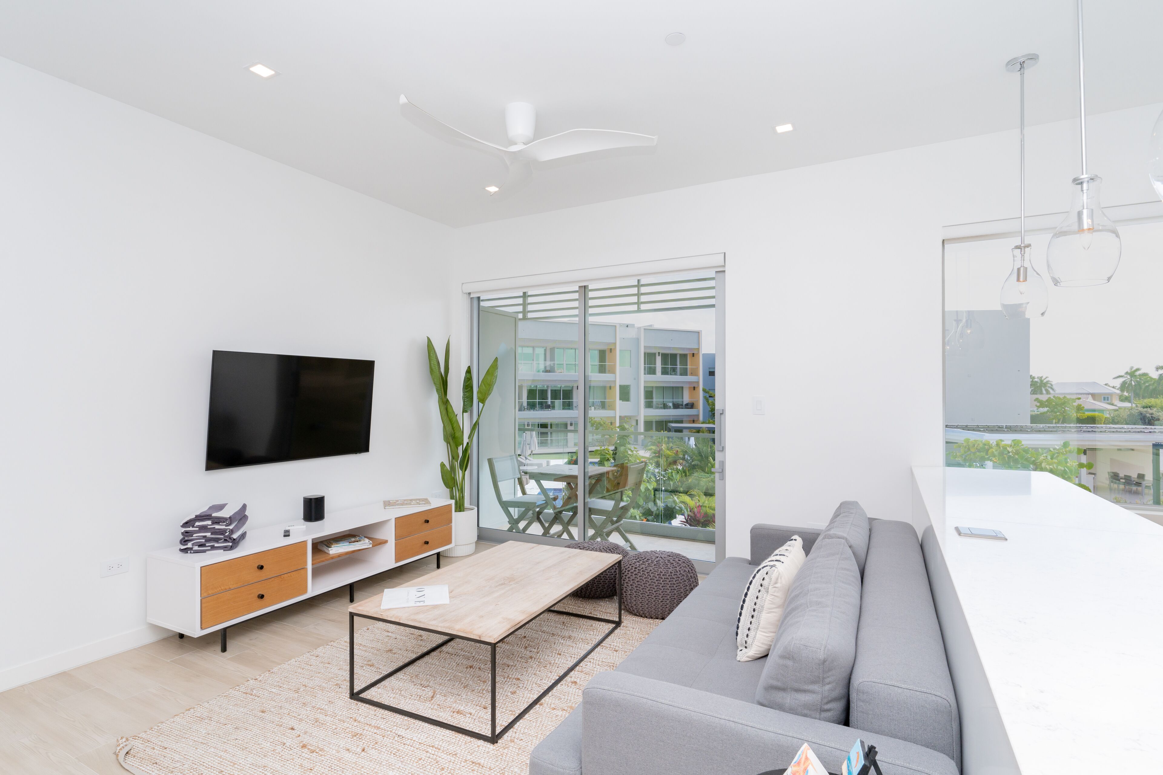 A modern living room with a flat-screen TV, a sofa, a coffee table, and a dining area with a glass table and chairs.