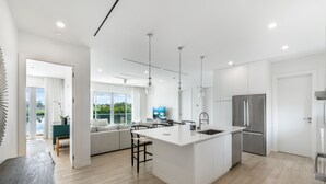 A modern kitchen with a central island, stainless steel appliances, and a view to the outdoors. - ONE Canal Point (Seven Mile Beach)