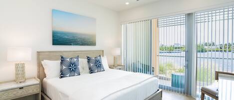 Une chambre d’hôtel moderne dotée d’un grand lit, d’une table de chevet, d’un bureau et offrant une vue sur l’extérieur grâce à de grandes fenêtres.