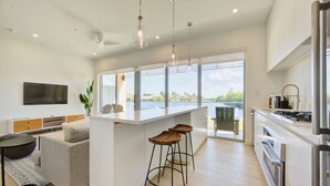 A modern kitchen with a central island, bar stools, a flat-screen TV, and large windows offering a view of the outdoors. - ONE Canal Point (Seven Mile Beach)