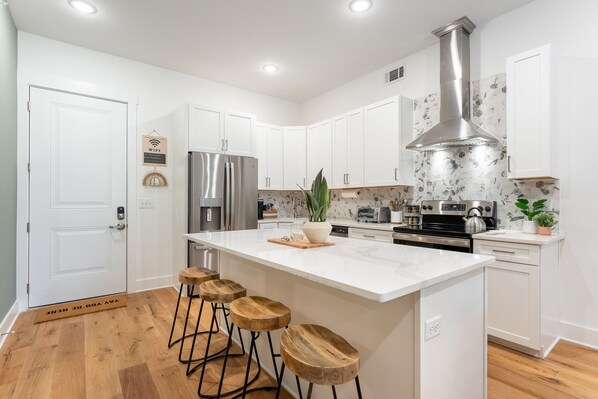 Una cocina moderna con armarios blancos, una campana extractora de acero inoxidable y una isla central con taburetes.