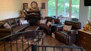 Ein geräumiges Wohnzimmer mit Ledersofas, einem Kamin und großen Fenstern mit Blick ins Freie.