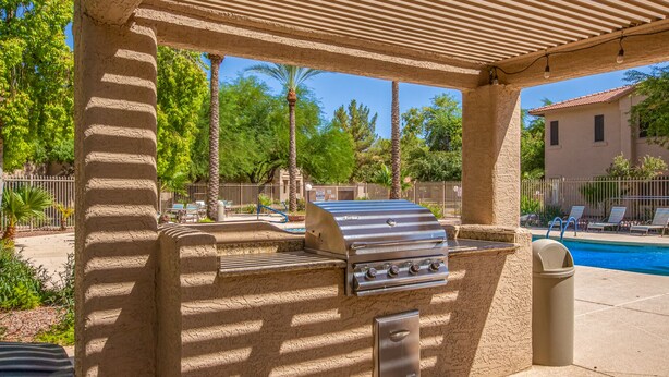 Un área de parrilla al aire libre con piscina al fondo.