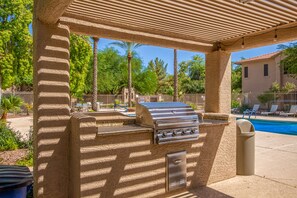 Un espace barbecue extérieur avec une piscine en arrière-plan.