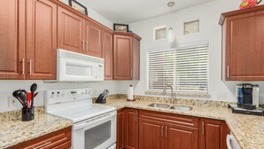 Una cocina con armarios de madera, estufa blanca, microondas, lavaplatos y una ventana con persianas.