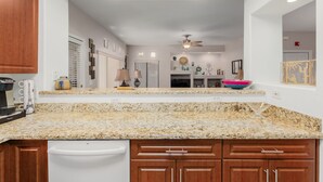 Una cocina con encimeras de granito, armarios de madera y lavavajillas blanco.